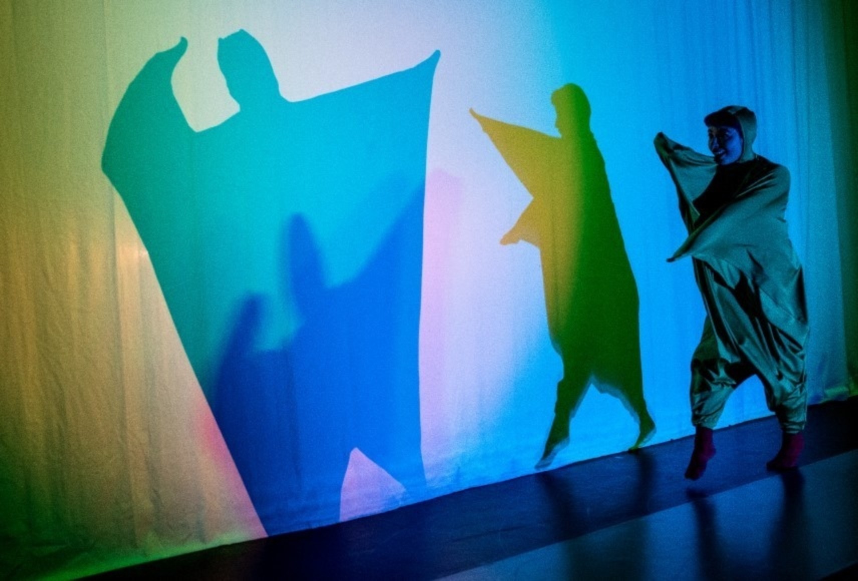 Une danseuse crée des ombres bleues et jaune sur un voile tendu.