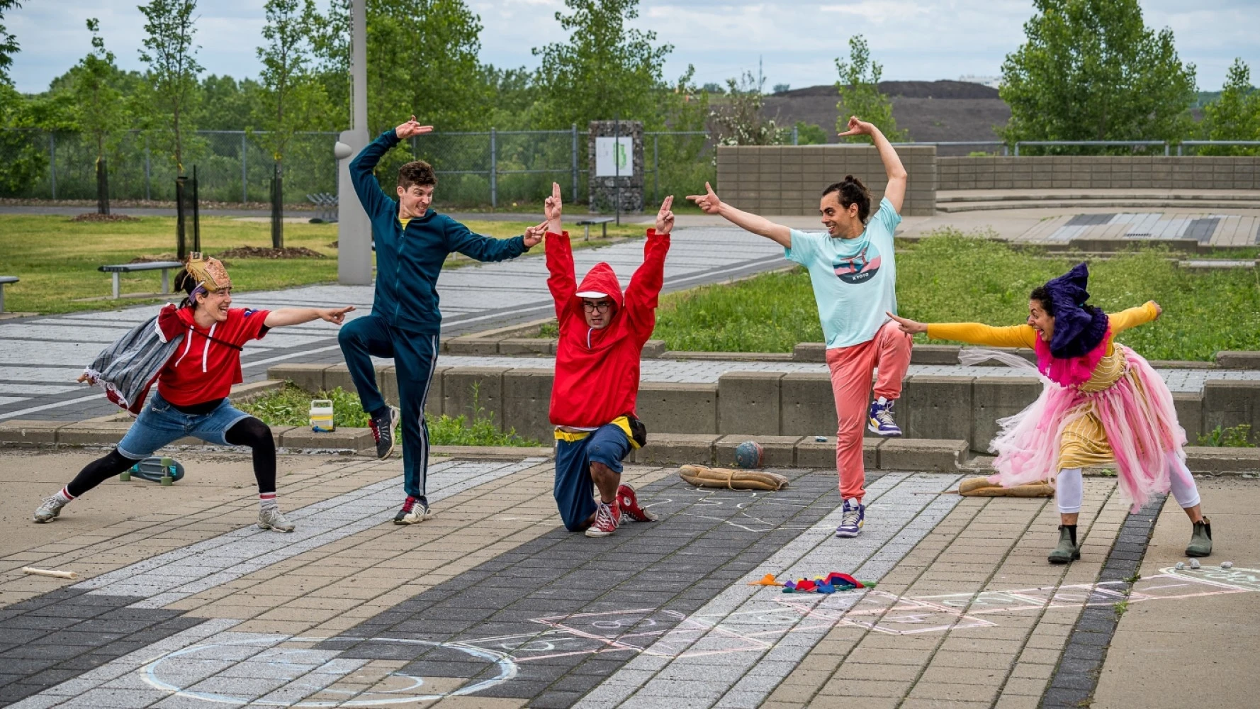 Photo en extérieur urbain d'un groupe de cinq comédiens et comédiennes, portant des habits colorés. Ils prennent des poses dynamiques et ont des visages expressifs.