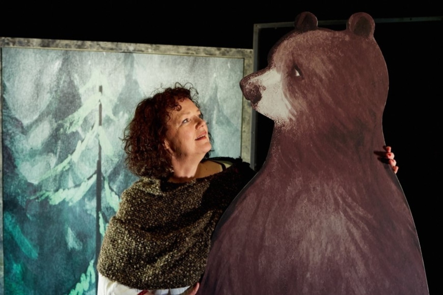 Jasmine regarde le gros ours, une main posée sur son épaule. Les deux sont de profil et se fond face, devant une illustration de forêt.